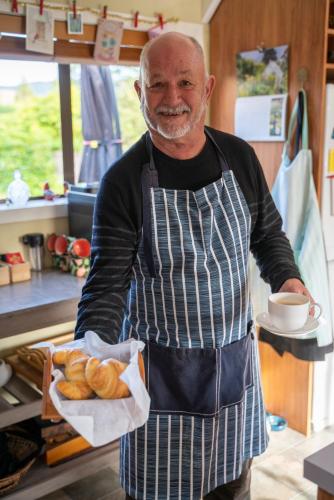 a man in a kitchen holding a tray of pastries at Alpine Rock B&B in Te Anau
