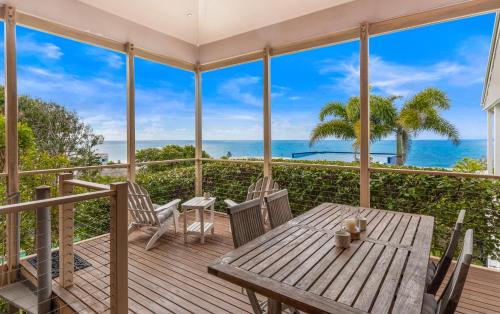 a porch with a wooden table and chairs and the ocean at Beachside Escape, Sunshine Beach in Sunshine Beach