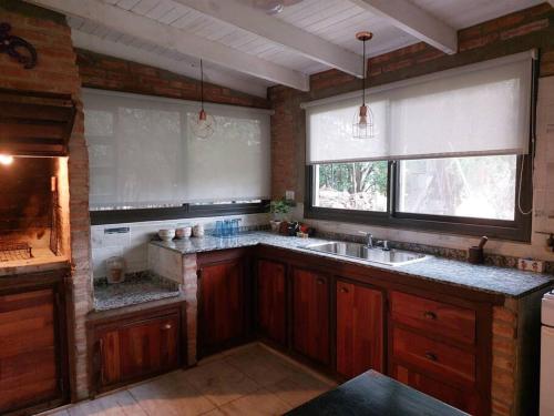 cocina con armarios de madera, fregadero y 2 ventanas en Cardozo House, casa de campo en Villa Dolores