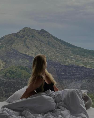 a woman sitting on a bed looking at a mountain at Devanora Hotel & Resto in Kintamani