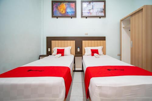 two beds in a room with red and white sheets at RedDoorz Syariah near Danau Lut Tawar Takengon in Takengon