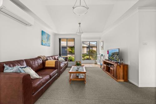 a living room with a brown leather couch and a tv at Coastal Villa by Experience Jervis Bay in Vincentia