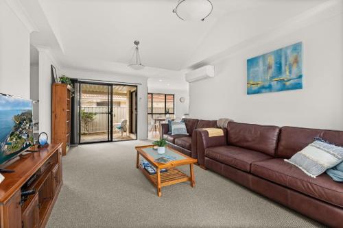 a living room with a brown couch and a table at Coastal Villa by Experience Jervis Bay in Vincentia