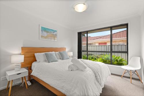 a white bedroom with a bed and a window at Coastal Villa by Experience Jervis Bay in Vincentia