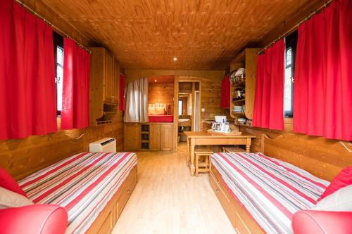 a room with two beds and a kitchen with red curtains at Roulottes et Cabanes de Saint Cerice in Vogüé