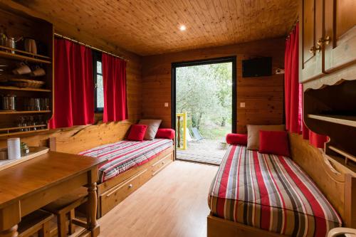 a room with two beds in a cabin with red curtains at Roulottes et Cabanes de Saint Cerice in Vogüé