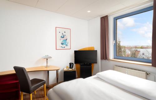 una camera d'albergo con letto, scrivania e finestra di Mainstreet Hotel a Dietzenbach