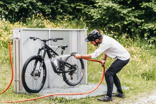un uomo sta lavando una bicicletta con un tubo di Peaks Place Apartments & SPA a Laax