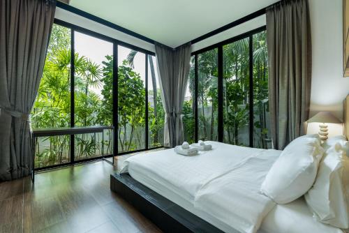 a bedroom with a large bed and large windows at Baan Bua BT17 by Villacarte in Nai Harn Beach