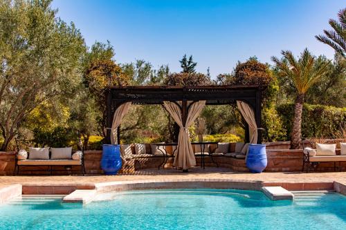 een zwembad met een prieel en een tafel en stoelen bij Villa Ferme de Coco in El Caïd Omar