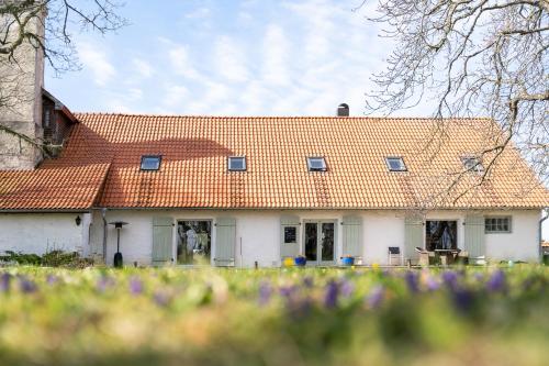 a white house with an orange roof with purple flowers at Dagen Haus Guesthouse in Orjaku