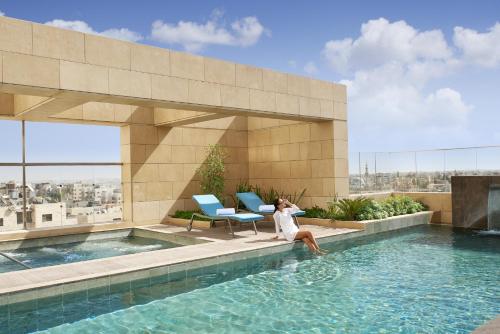 Eine Frau, die am Rande eines Swimmingpools auf einem Gebäude sitzt. in der Unterkunft Fairmont Amman in Amman