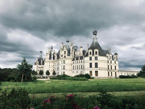 un grand château blanc avec un ciel nuageux dans l'établissement Domaine Oranga, un design élégant au luxe épuré près des Châteaux de la Loire, à Lanthenay