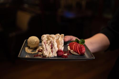 a person holding a plate with a piece of cake and strawberries at Errigal Country House Hotel in Cootehill