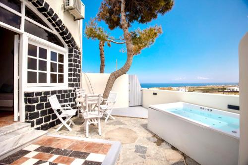 un patio con bañera de hidromasaje, mesa y sillas en Dawn Suites Santorini, en Vourvoúlos