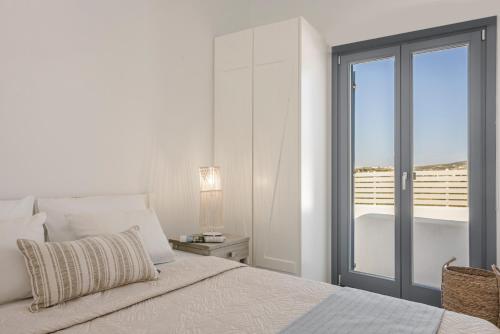 a white bedroom with a bed and a balcony at Pebble Summer House in Kampos Paros