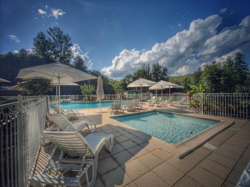a swimming pool with chairs and umbrellas next to a pool at hôtel gites le clos du moulin in Terrasson-Lavilledieu