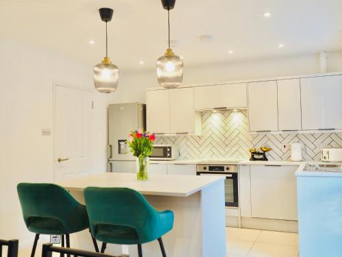 a kitchen with white cabinets and a table with green chairs at Luxurious Detached Bungalow with Private Parking in Farnborough