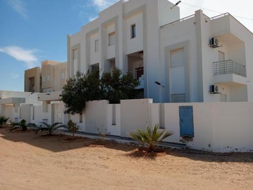 - un bâtiment blanc sur la plage à côté d'une clôture dans l'établissement Résidence Inès Djerba Appartement de Luxe, à Houmt Souk