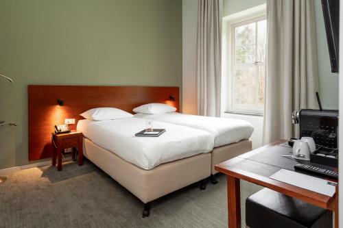 アメルスフォールトにあるLeerhotel Het Kloosterのベッドとデスクが備わるホテルルームです。