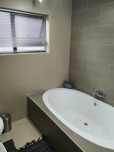 a white bath tub in a bathroom with a window at Posh 3 bedroomed guesthouse in Hillside with pool - 2039 in Bulawayo