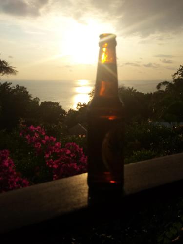 a bottle of beer sitting on a ledge with the sunset at Coyaba Tropical Elegant Adult Guesthouse in Manuel Antonio