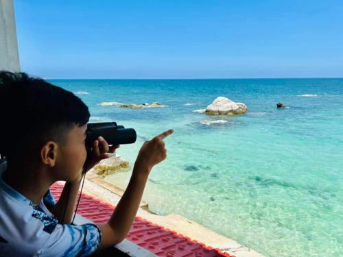 a boy taking a picture of the ocean with a camera at Mũi Dinh Hotel in Phan Rang