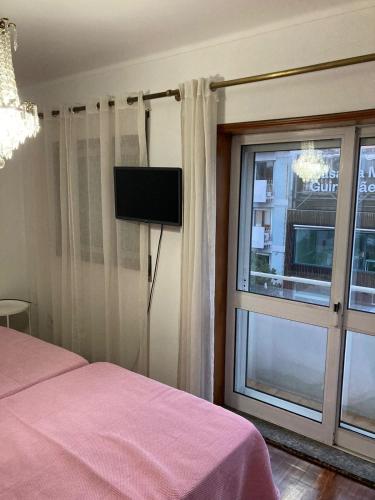 a bedroom with a bed and a window with a tv at Hospedaria Cidade Berço in Guimarães
