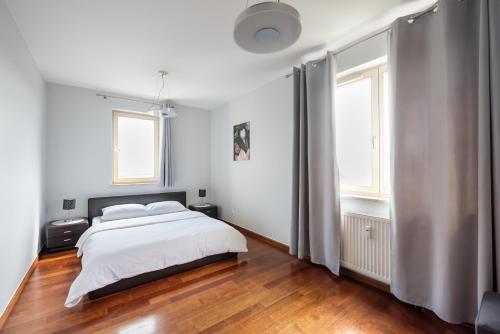 a white bedroom with a bed and two windows at Mokotów Open Business Apartment in Warsaw