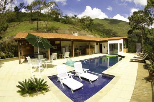 a villa with a swimming pool with chairs and a house at Pousada Alto Itaipava in Itaipava