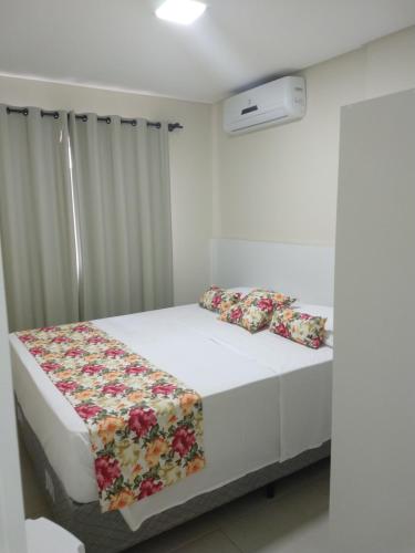 a white bedroom with a bed with a floral blanket at Pousada Bella Bombinhas - Pé na areia in Bombinhas