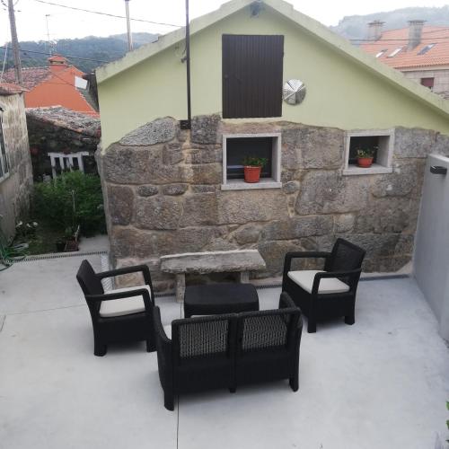 a patio with chairs and a table and a stone wall at A CASIÑA DA EIRAVELLA in Hio
