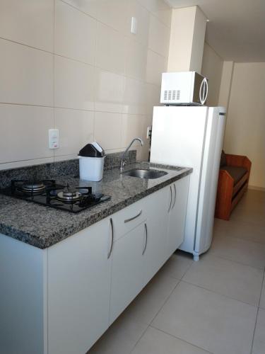 a white kitchen with a sink and a refrigerator at Pousada Bella Bombinhas - Pé na areia in Bombinhas