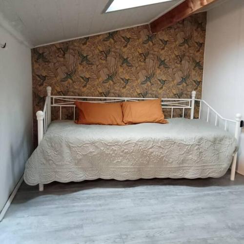 a white bed with an orange pillow on a wall at LE COLIBRIS in Issoire