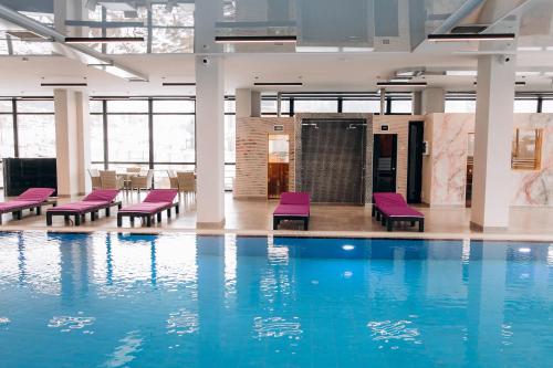 Kasimir Resort Hotel & SPA في بوكوفِل: حمام سباحة مع كراسي أرجوانية في مبنى