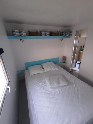 une petite chambre avec un lit avec des draps blancs et des oreillers dans l'établissement Mobil home 4 couchages, à Mimizan