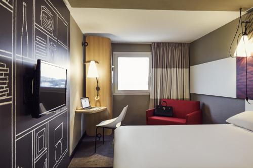 a hotel room with a bed and a red chair at ibis Toulon La Valette in La Valette-du-Var