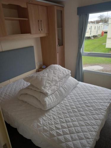 1 cama con sábanas blancas en un dormitorio con ventana en Sunny Hunny Manor Park Caravan, en Hunstanton