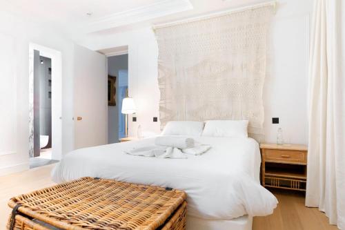 a white bedroom with a large bed and a wicker stool at Knightsbridge - Sumptuous Flat - Hyde Park in London