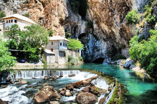 a river with a building in the middle of a mountain at Hotel Argentum in Mostar
