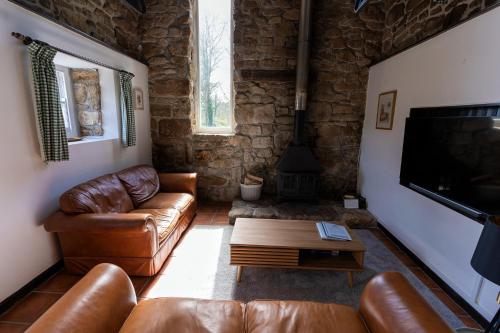 a living room with leather furniture and a flat screen tv at Beautiful Cornish barn in the stunning Lamorna valley with large garden in Paul