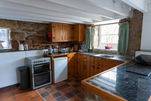 una cocina con armarios de madera y una pared de piedra. en Beautiful Cornish barn in the stunning Lamorna valley with large garden, en Paul
