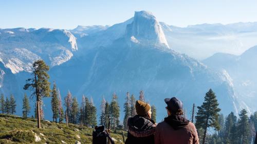 two people sitting on a hill looking at a mountain at AutoCamp Yosemite in Midpines