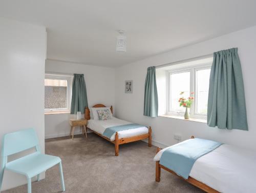 a bedroom with two beds and a chair and windows at Ysgo - 6 Ty'n Don in Abersoch