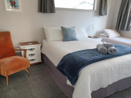a bedroom with two beds and a chair and a window at Kiwiana Gem in Reefton
