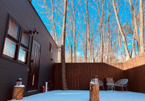 a black house with chairs and a fence and trees at サウナ・ジャグジー・完全貸し切りという贅沢　大人の秘密基地　Tiny Cabin TATEGU#02 in Miyota
