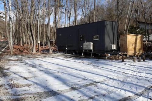 a black trailer sitting in the snow next to trees at サウナ・ジャグジー・完全貸し切りという贅沢　大人の秘密基地　Tiny Cabin TATEGU#02 in Miyota