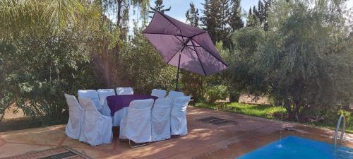stół i krzesła z parasolem przy basenie w obiekcie villa Marrakech raja w Marakeszu