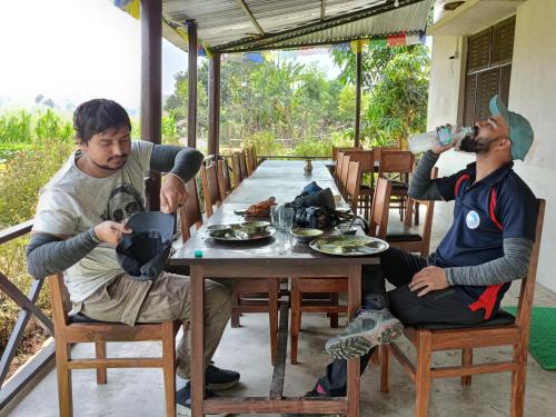 two men sitting at a table drinking from water bottles at Bardiya Eco Safari Homestay in Bhurkīā