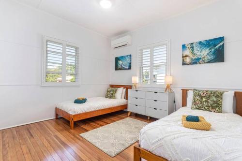 a bedroom with two beds and a dresser and two windows at Stylish 1950s Moffat Beach House in Caloundra